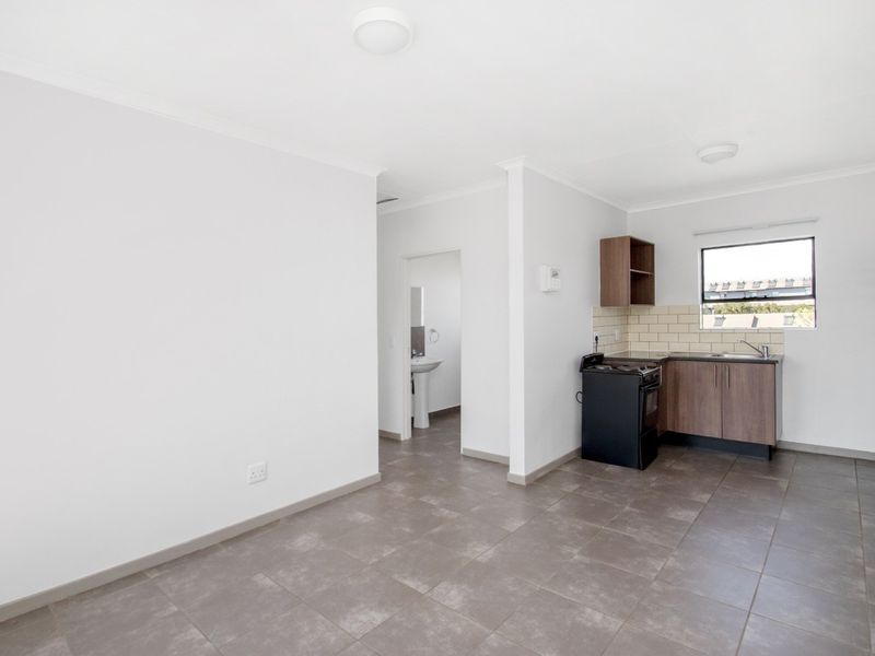 An open-plan living area featuring tiled flooring, a compact kitchen with built-in cabinetry, and a view into an adjacent bathroom.