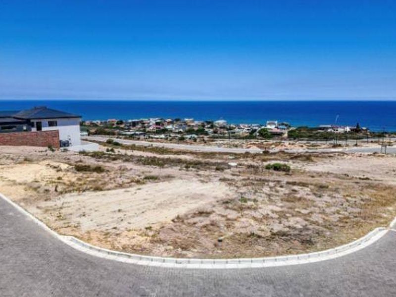 An elevated aerial view of a vacant residential plot situated in a coastal estate, featuring paved road access and expansive ocean views.