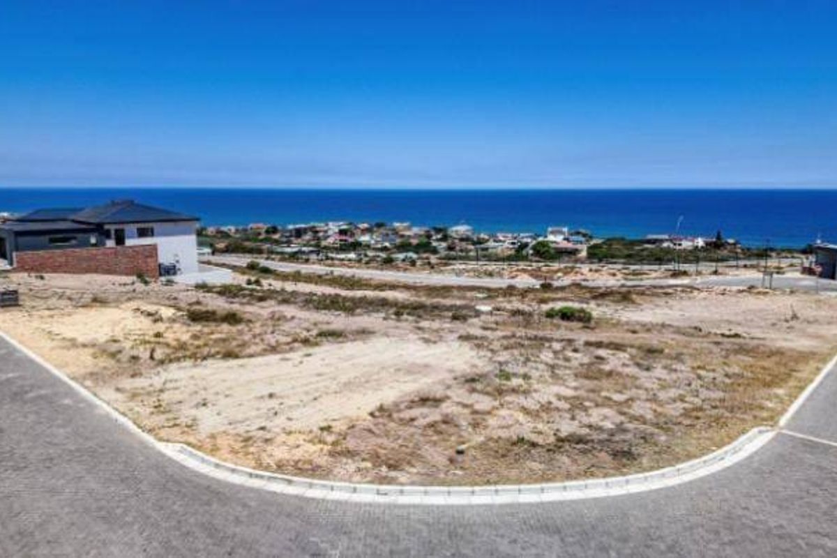 An elevated aerial view of a vacant residential plot situated in a coastal estate, featuring paved road access and expansive ocean views.
