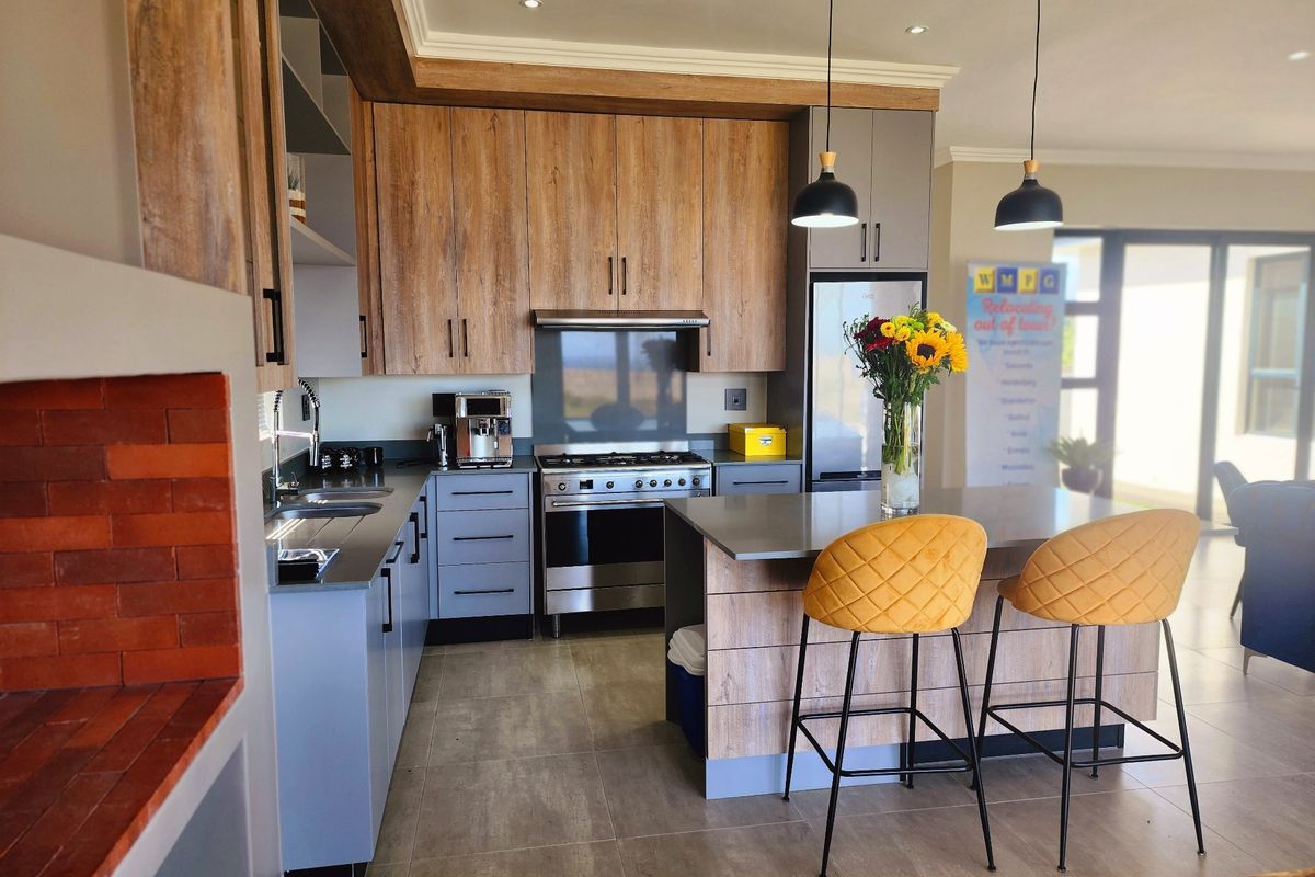 Modern kitchen featuring wood-grain and grey cabinetry, a central island with stone countertops, stainless steel appliances, and recessed lighting.