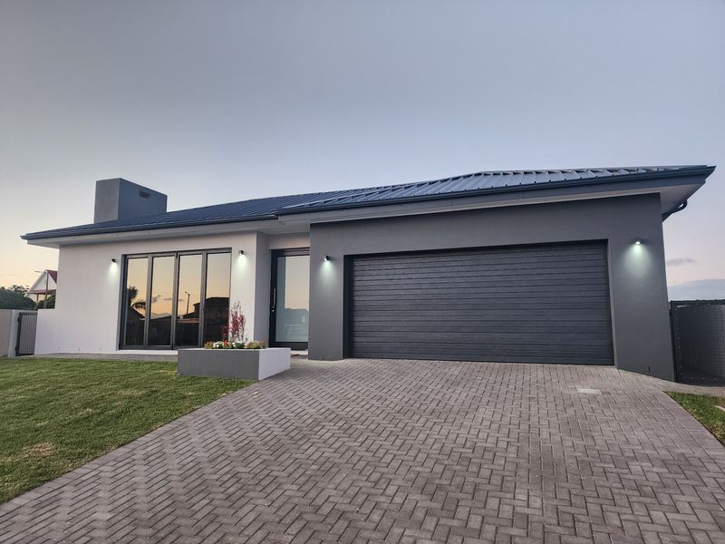 Modern single-story home exterior featuring a paved driveway, integrated garage, contemporary dark metal roof, and large glass sliding doors.