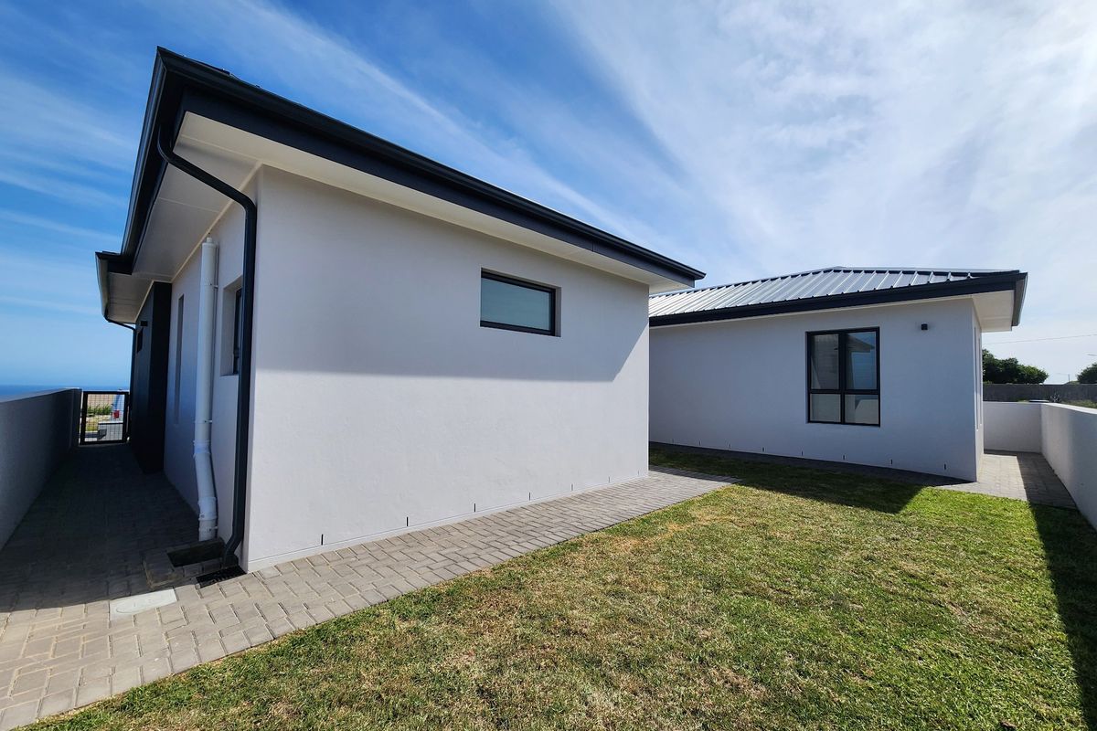 A view of the rear exterior of the property featuring modern white facades, metal roofing, and a neat paved walkway alongside a small lawn.