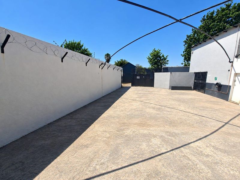 A secure, paved commercial yard area featuring high perimeter walls with barbed wire and gated access, suitable for parking or storage.