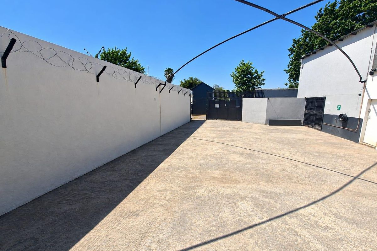 A secure, paved commercial yard area featuring high perimeter walls with barbed wire and gated access, suitable for parking or storage.