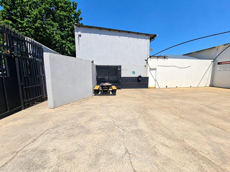 A paved rear commercial yard area featuring perimeter walls, metal security gates, and basic utility access points.