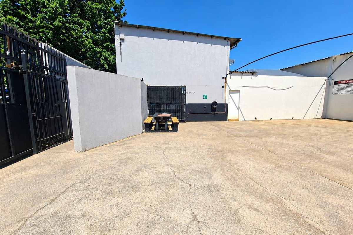 A paved rear commercial yard area featuring perimeter walls, metal security gates, and basic utility access points.
