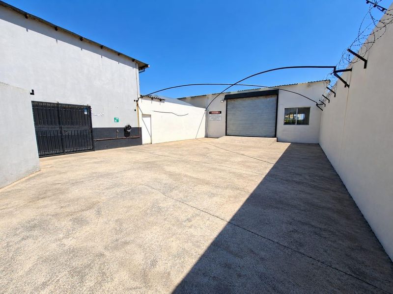 A secure commercial yard featuring a concrete surface, perimeter wall with razor wire, and a roller shutter door for loading access.