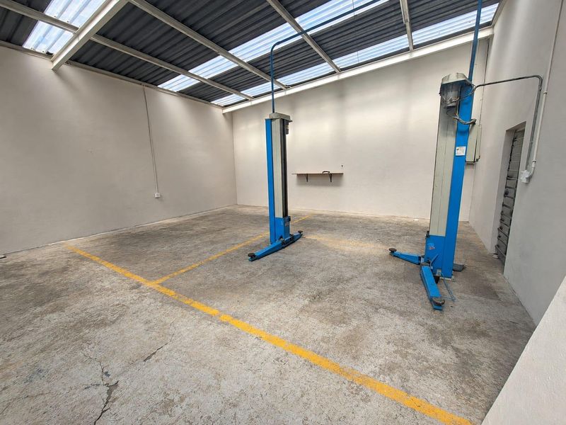 A functional commercial garage space featuring a built-in vehicle hoist, concrete flooring with painted markings, and a translucent roof for natural lighting.