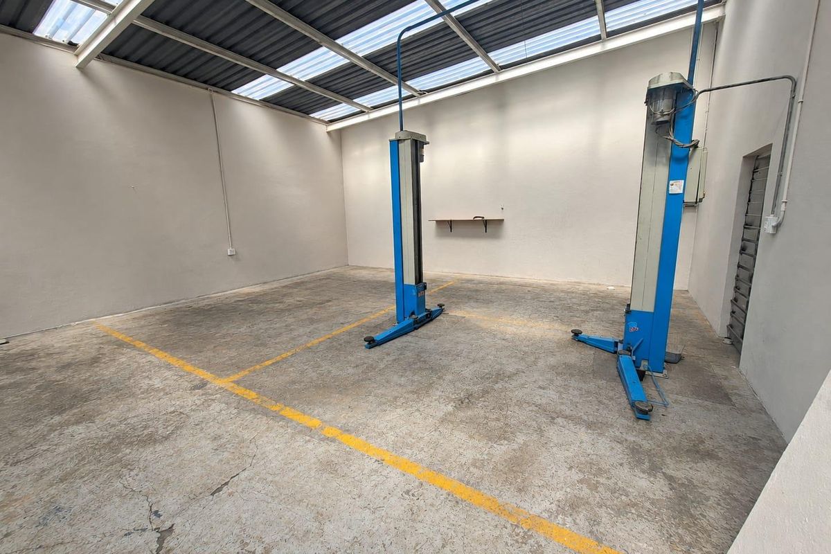 A functional commercial garage space featuring a built-in vehicle hoist, concrete flooring with painted markings, and a translucent roof for natural lighting.