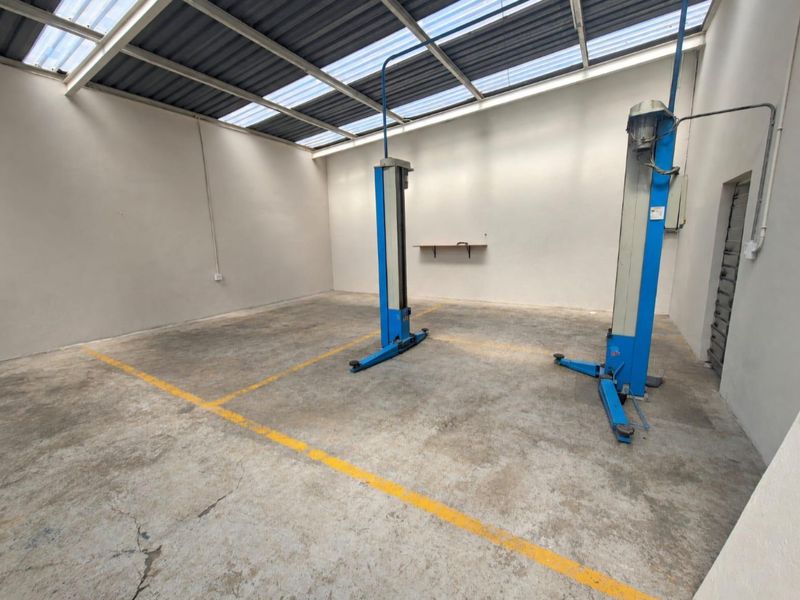 Commercial garage space featuring a two-post vehicle lift, concrete flooring with painted markings, and a translucent roof structure for natural lighting.