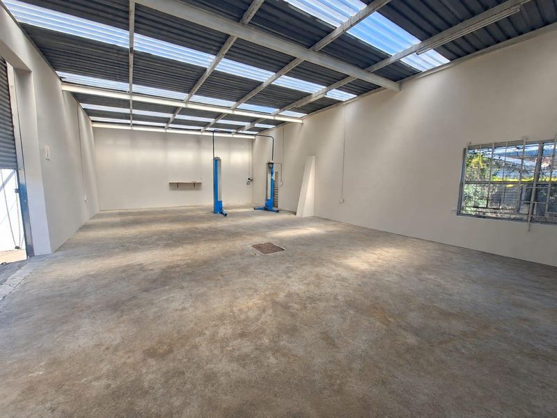 Spacious commercial garage or workshop area featuring a two-post vehicle lift, high ceilings with translucent roof panels, and secure window access.