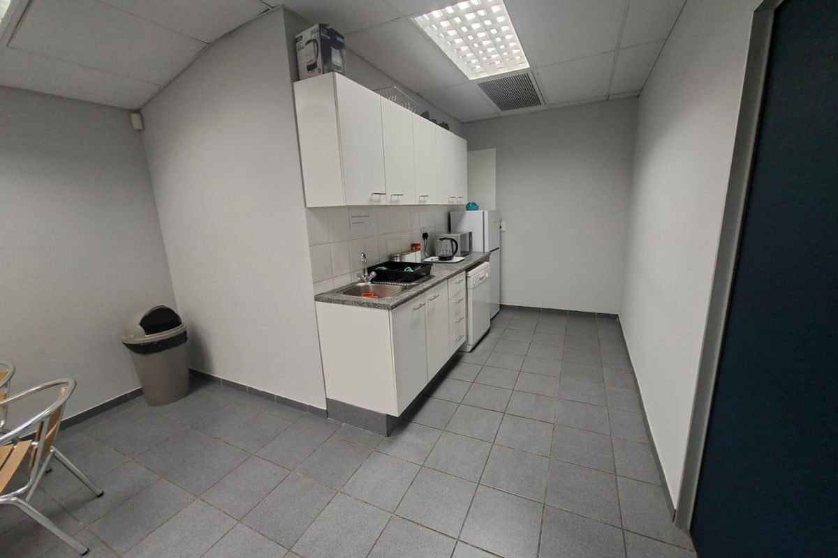 A functional commercial kitchenette featuring white cabinetry, a stainless steel sink, tiled flooring, and a drop ceiling with integrated lighting.