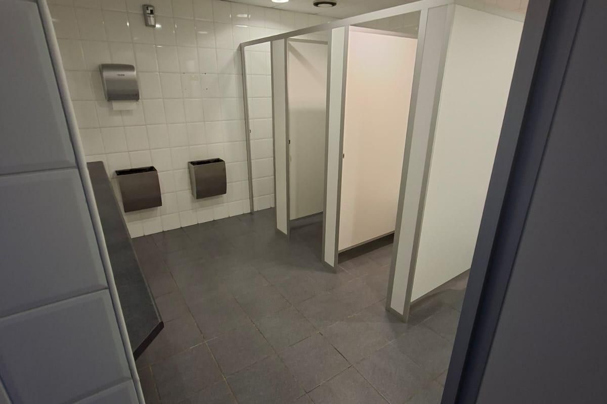 A functional commercial restroom featuring tiled walls and flooring, multiple toilet cubicles, and integrated stainless steel fixtures.