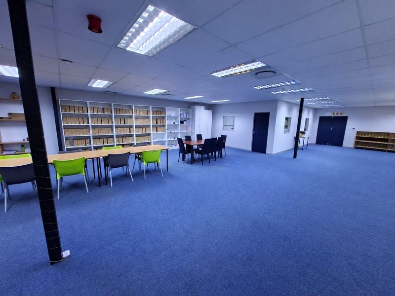 Spacious commercial office area featuring suspended ceilings, recessed lighting, blue carpeting, and extensive built-in shelving units for organized storage.