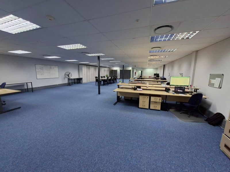 Spacious open-plan commercial office area featuring suspended ceilings, recessed lighting, blue carpeting, and integrated storage cabinetry.