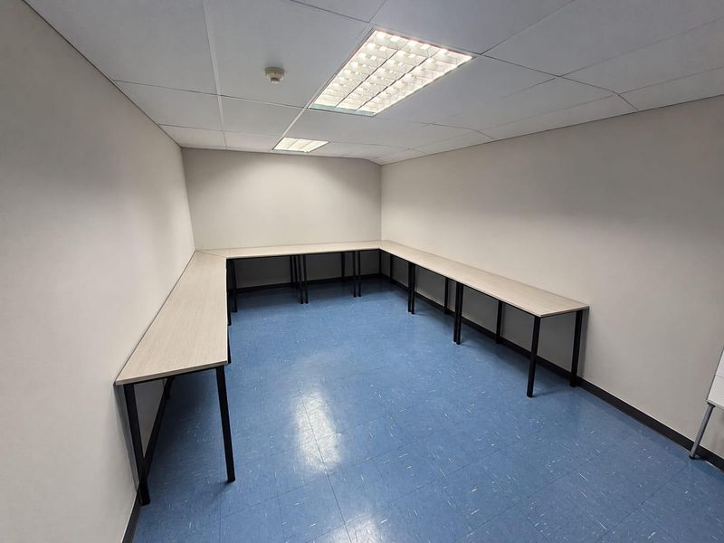 A functional, empty office space featuring durable vinyl flooring, recessed ceiling lighting, and integrated U-shaped desk surfaces.