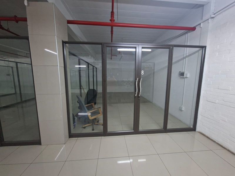 A vacant commercial office space featuring glass partitions, tiled flooring, and an industrial-style exposed ceiling with fire sprinkler systems.