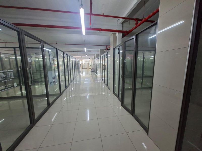 A modern commercial hallway featuring glass-partitioned office units, polished tile flooring, and exposed industrial-style fire sprinkler piping.