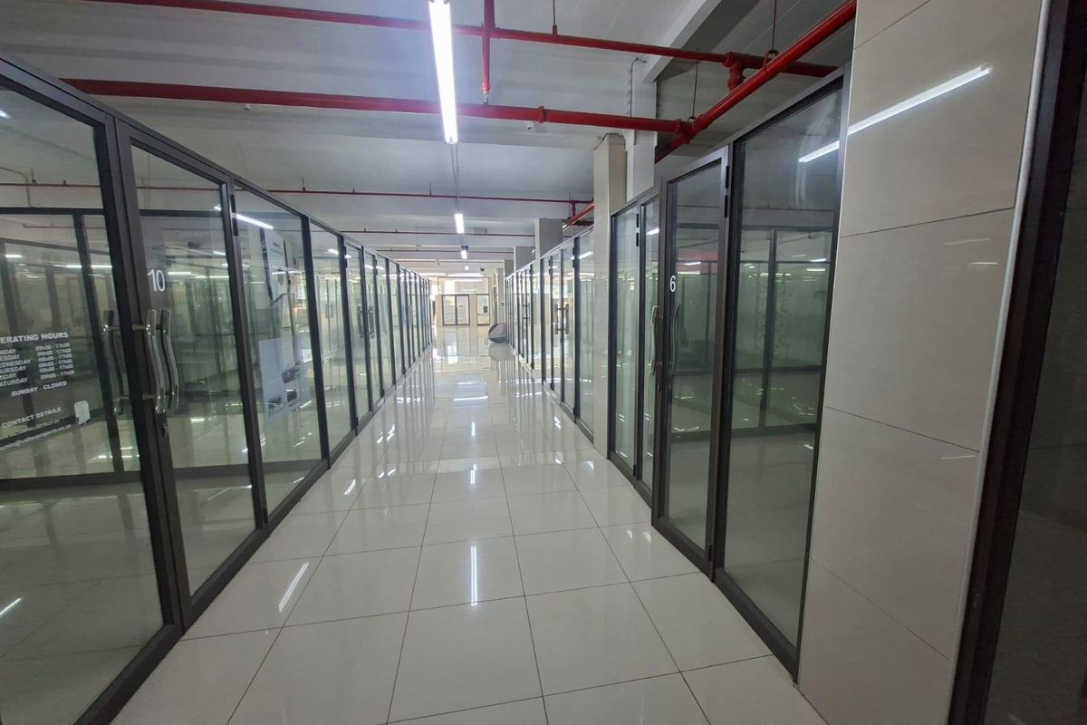A modern commercial hallway featuring glass-partitioned office units, polished tile flooring, and exposed industrial-style fire sprinkler piping.