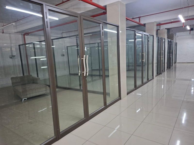 A commercial office space featuring multiple glass-partitioned rooms, tiled flooring, and exposed industrial-style fire sprinkler piping.