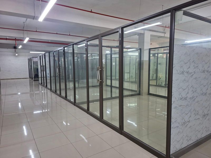 Modern commercial office space featuring glass partitioned rooms, polished ceramic tile flooring, and an open-plan industrial ceiling design with integrated lighting.