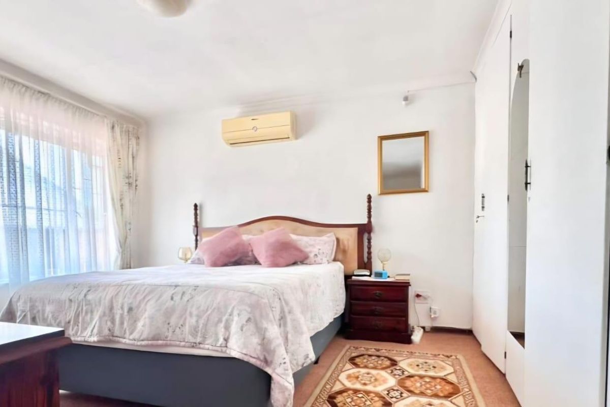 A well-lit bedroom featuring built-in cupboards, carpeted flooring, and a wall-mounted split-system air conditioning unit.