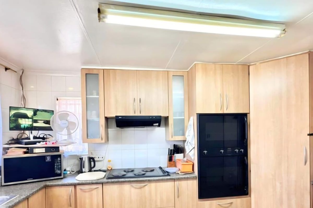 A functional kitchen featuring light wood-finish cabinetry, granite countertops, a built-in oven, and an electric hob with an integrated extractor fan.