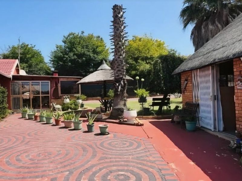 A rear courtyard area featuring a brick-built structure with a thatched roof, paved flooring, and an outdoor entertainment lapa.