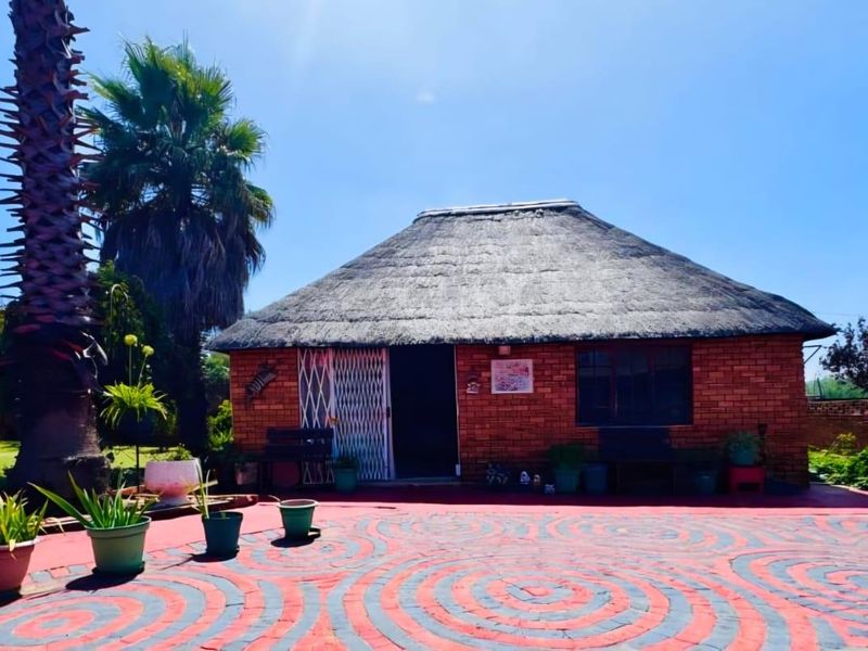 A detached brick building with a traditional thatch roof, featuring a patterned paved patio area in a garden setting.
