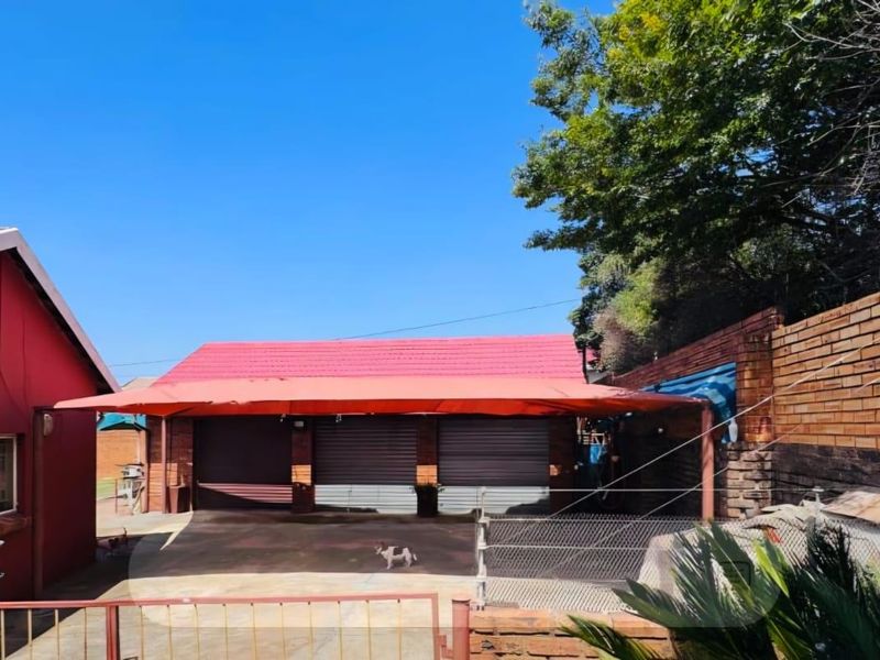 Rear exterior view showing a triple garage with metal roller doors, a covered carport area, and a brick retaining wall.