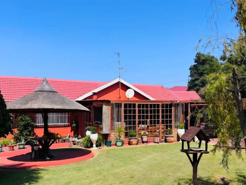 Rear view of the property featuring a red tiled roof, an enclosed patio area, and a thatched gazebo set within a landscaped garden.