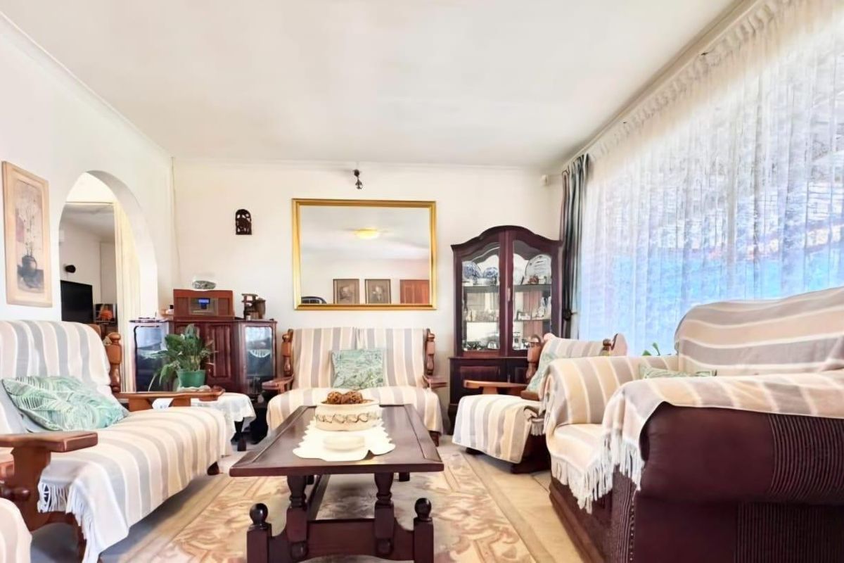 A spacious living room featuring a large window, coved ceilings, and an arched entryway leading to adjacent living areas.