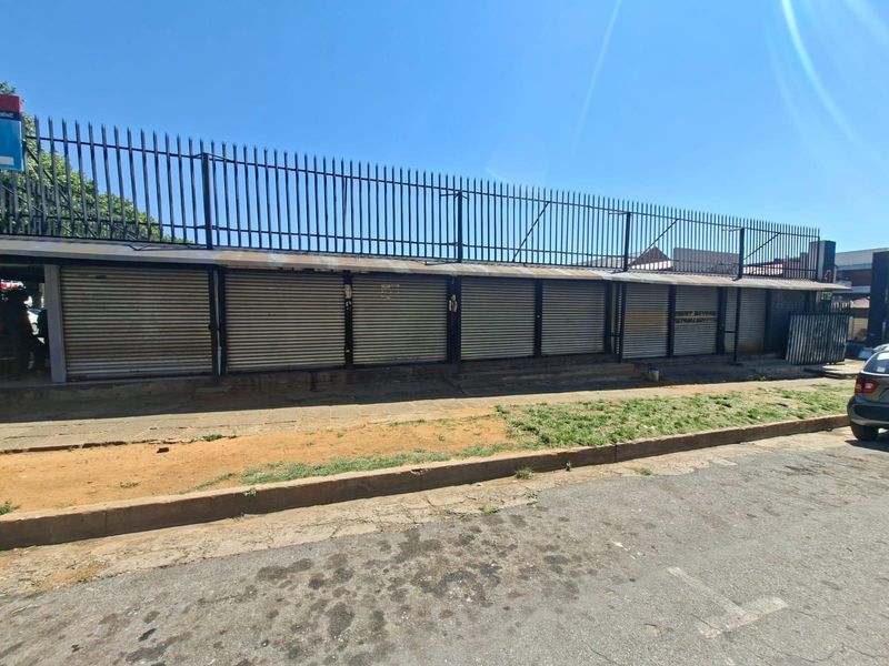 Commercial street-front property featuring a row of secure metal roller shutter doors and perimeter security fencing.