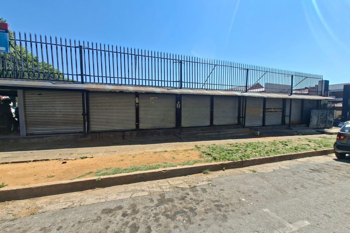 Commercial street-front property featuring a row of secure metal roller shutter doors and perimeter security fencing.