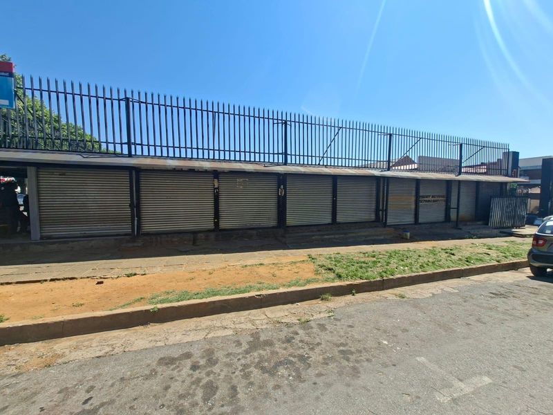 Commercial street-facing facade featuring multiple metal roller shutter doors and perimeter security fencing.