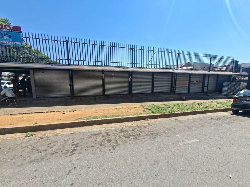 Commercial street-facing facade featuring multiple metal roller shutter doors and security fencing along the perimeter.