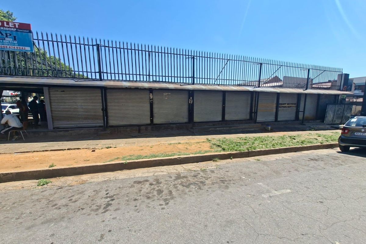 Commercial street-facing facade featuring multiple metal roller shutter doors and security fencing along the perimeter.