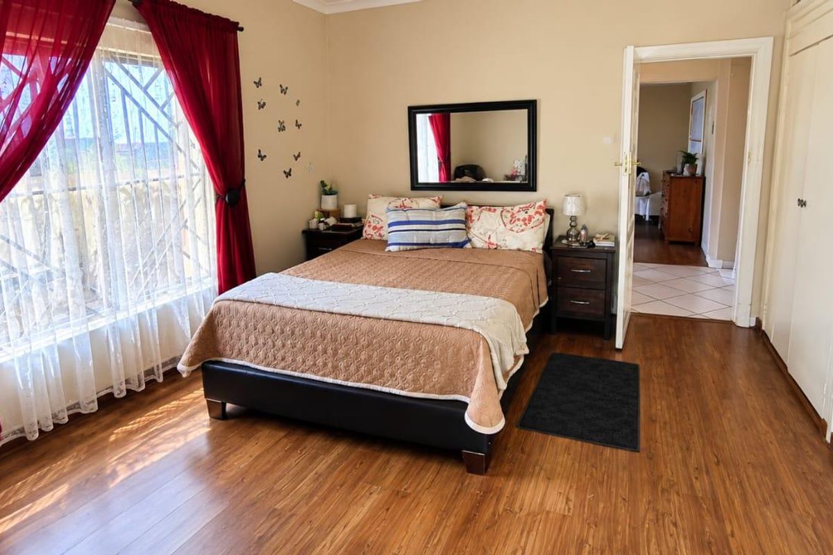 A well-lit bedroom featuring laminate flooring, built-in cupboards, and security bars on the window, offering a functional and comfortable living space.