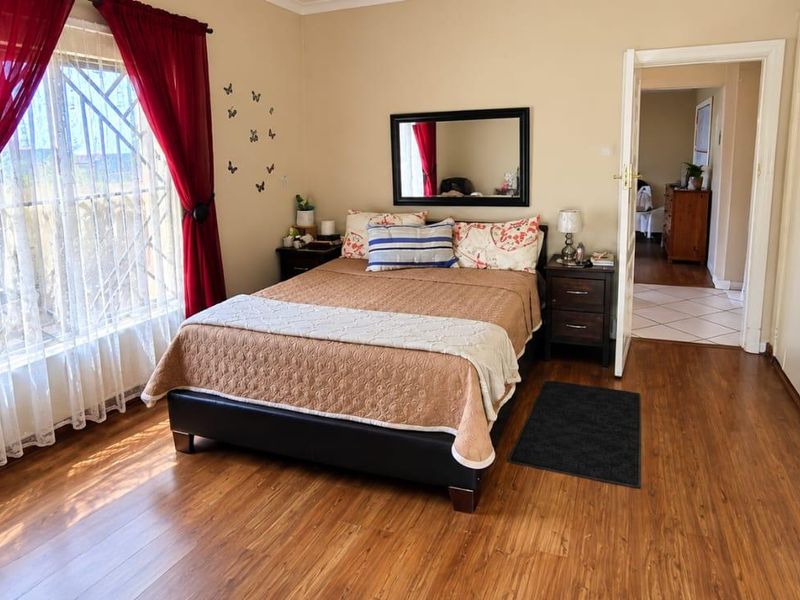A well-lit bedroom featuring laminate flooring, built-in cupboards, and security bars on the window, offering a functional and comfortable living space.