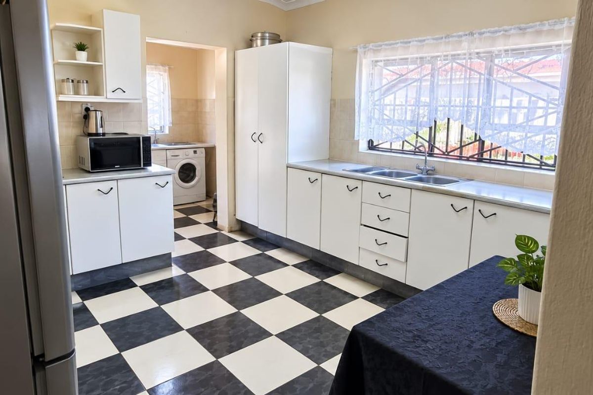 A functional kitchen featuring white cabinetry, a double sink, and classic black and white checkered floor tiles, with an adjoining laundry area.