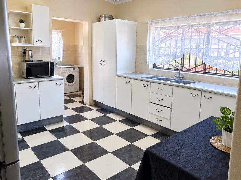 A functional kitchen featuring white cabinetry, a double sink, and classic black and white checkered floor tiles, with an adjoining laundry area.