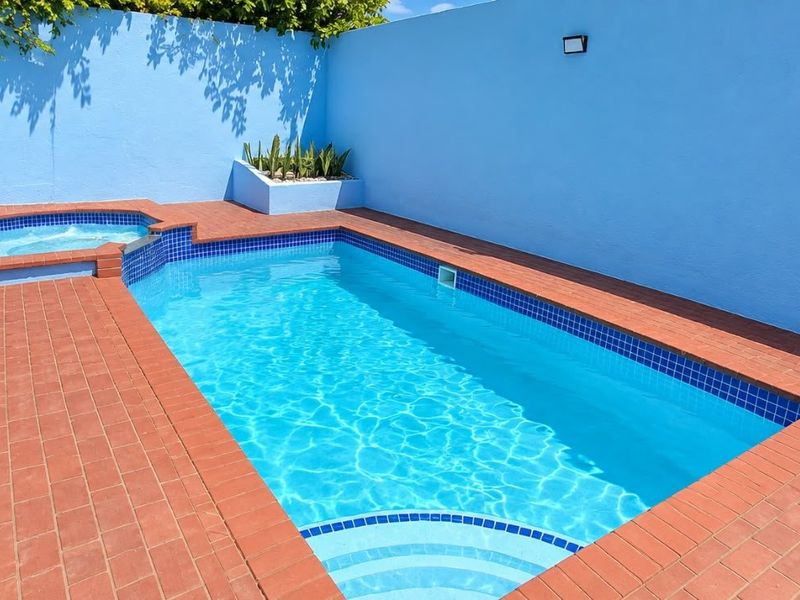 A private outdoor pool area featuring a swimming pool with an integrated spa, surrounded by brick paving and enclosed by high masonry walls.