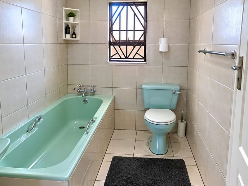 A functional bathroom featuring a pastel green bathtub and toilet, complemented by neutral wall and floor tiles and a secure window.