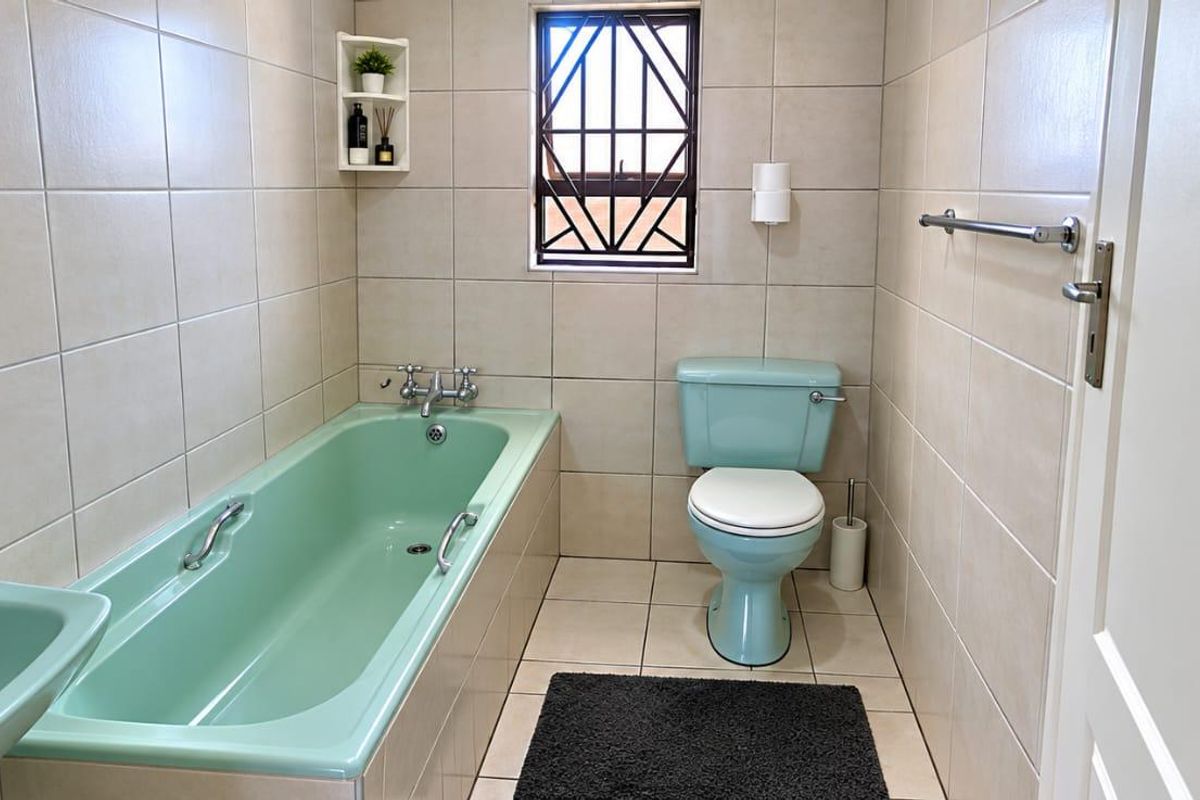 A functional bathroom featuring a pastel green bathtub and toilet, complemented by neutral wall and floor tiles and a secure window.