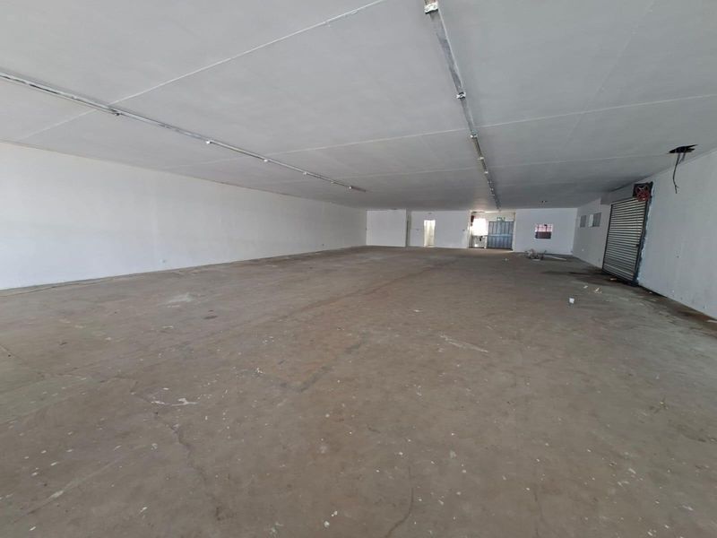 A large, open-plan commercial space featuring concrete flooring, roller shutter access, and overhead lighting tracks, suitable for various retail or industrial business applications.