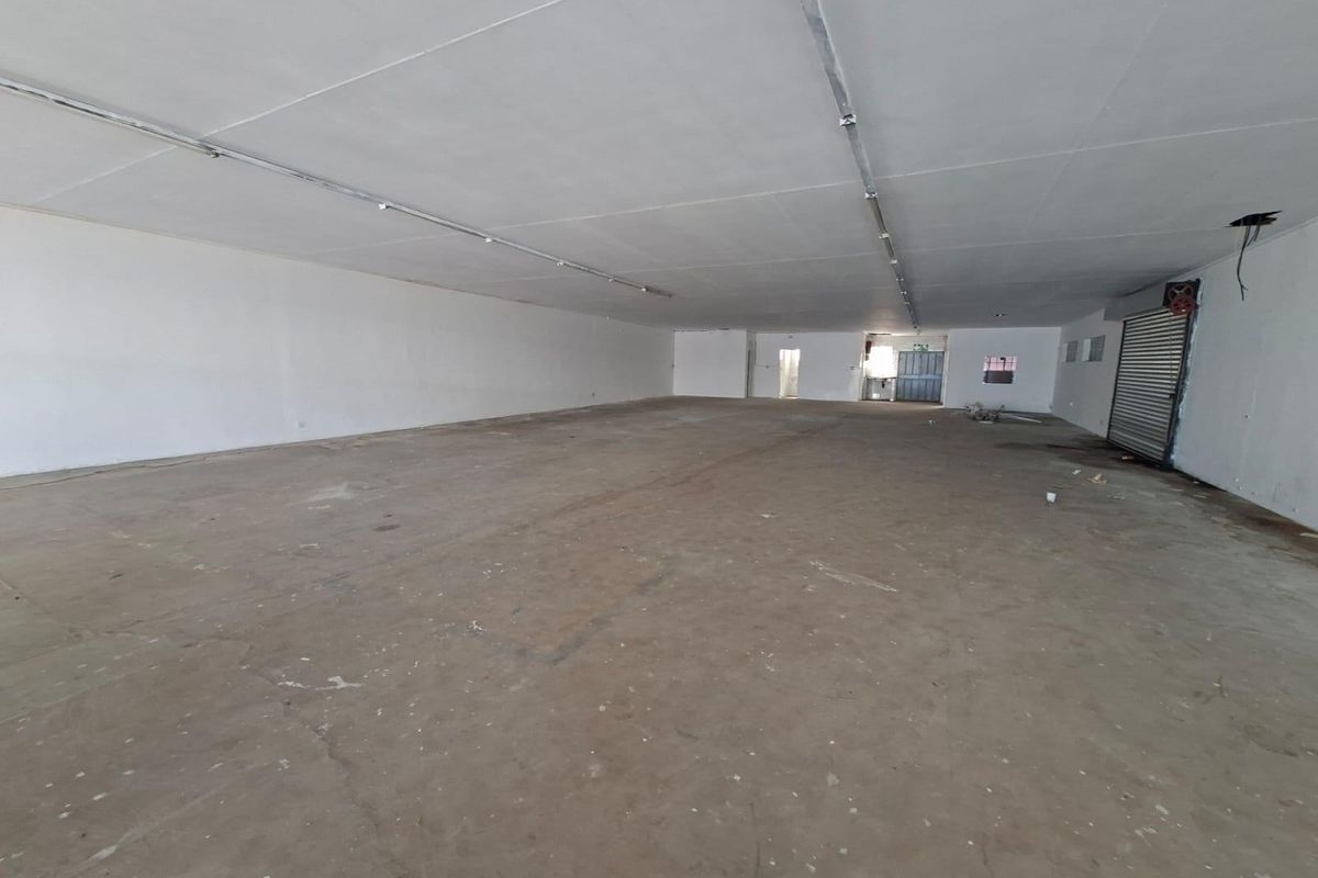A large, open-plan commercial space featuring concrete flooring, roller shutter access, and overhead lighting tracks, suitable for various retail or industrial business applications.