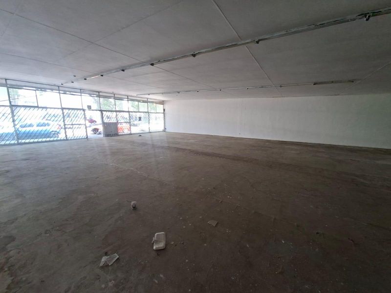 Spacious open-plan commercial retail space featuring a large glass storefront, security gate, and exposed concrete flooring, suitable for various business applications.