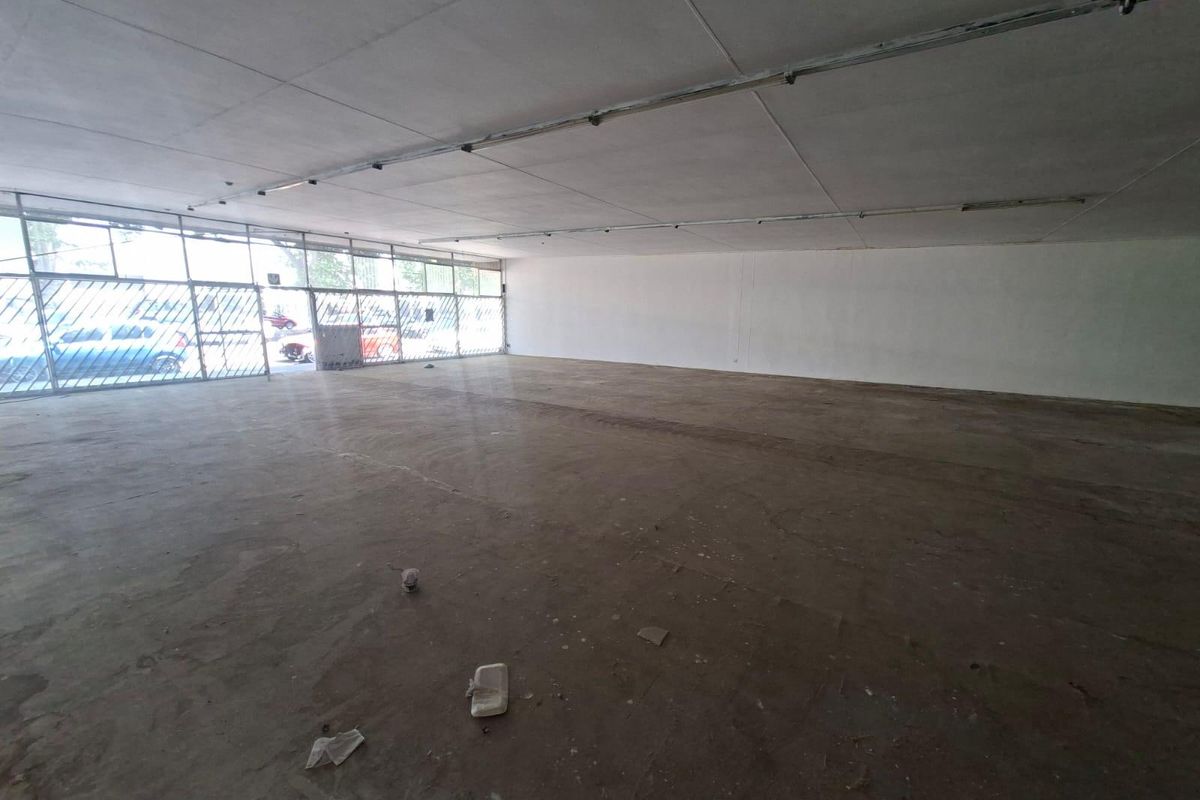 Spacious open-plan commercial retail space featuring a large glass storefront, security gate, and exposed concrete flooring, suitable for various business applications.