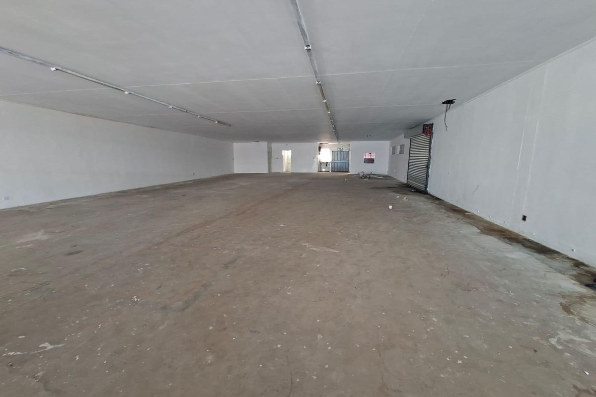 A large, open-plan commercial space featuring concrete flooring, fluorescent lighting, and a roller shutter door, suitable for various retail or industrial applications.
