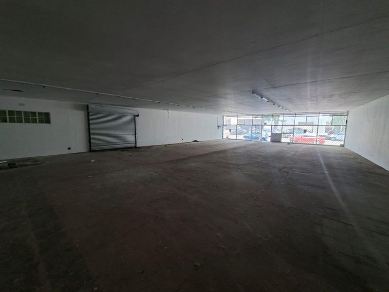 Spacious open-plan commercial unit featuring a large glass storefront, roller shutter door, and concrete flooring, suitable for various retail or office applications.